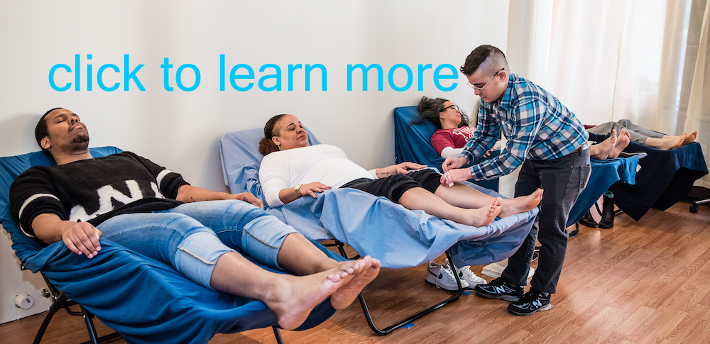Click to learn more blue text on wall in photo showing Oren Ren Pilinger Licensed Acupuncturist treating someone in a recliner while other people relax on other recliners in the treatment room at Boston Acupuncture Project in Hyde Park MA.
