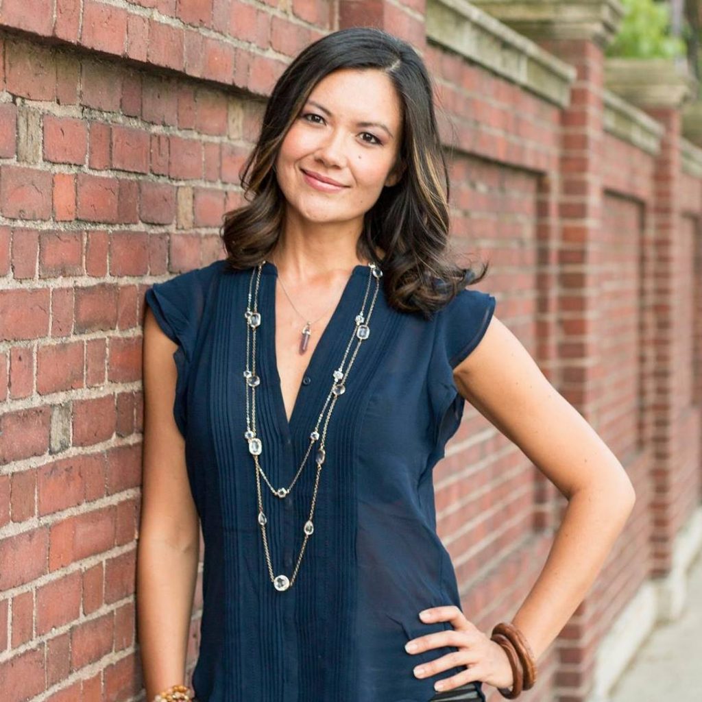 Nicole Brown portrait by Malka Ahmed Photography. Smiling woman leans against brick wall with hand on hip.