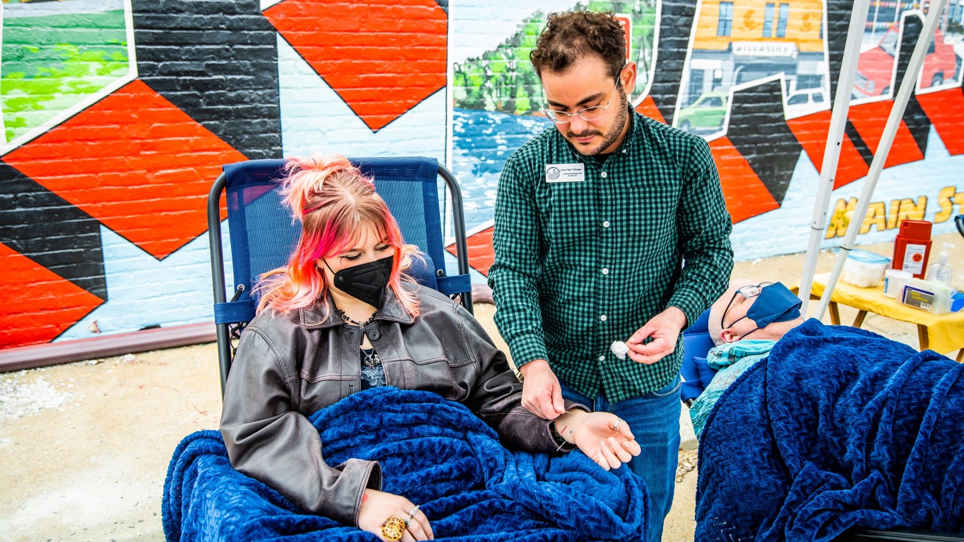 Licensed acupuncturist Ren treats a patient outdoors near the Hyde Park mural on the side of the clinic's Fairmount Ave building.